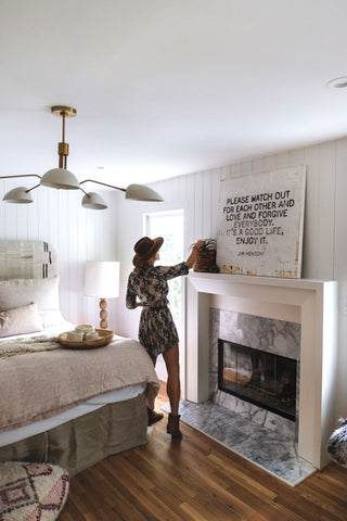 A woman standing in front of a bedroom fireplace, exuding warmth and comfort.