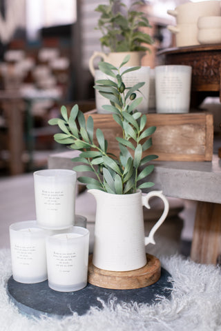 A table with a white pitcher, candles, and a plant.