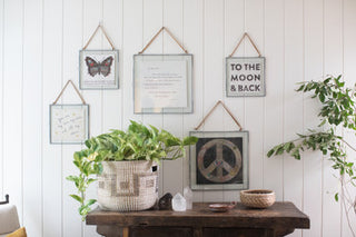 A wooden table adorned with a basket of plants and framed pictures, creating a serene and natural ambiance.