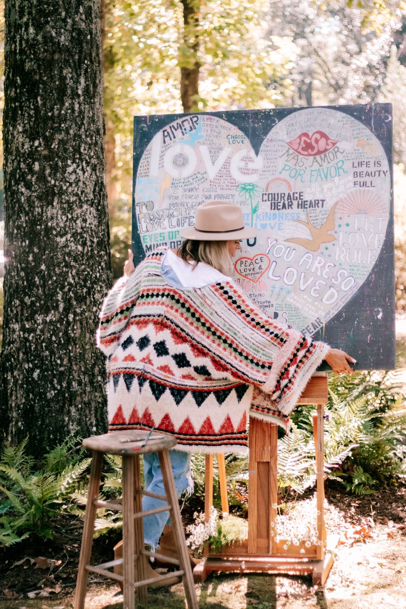 A woman painting a love heart on a canvas in the woods. Serene nature setting inspires artistic expression.