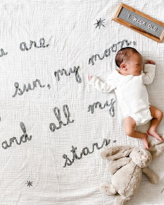 Newborn baby wrapped in a blanket with words written on it. 